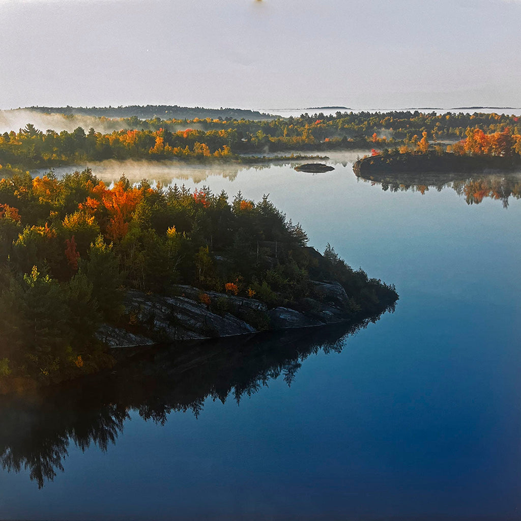Breathtaking autumn aerial landscape of a tranquil lake surrounded by a forest of colorful orange and green trees, with a gentle mist rising above the water. Keywords: fall foliage calendar, autumn scenery, aerial photography.