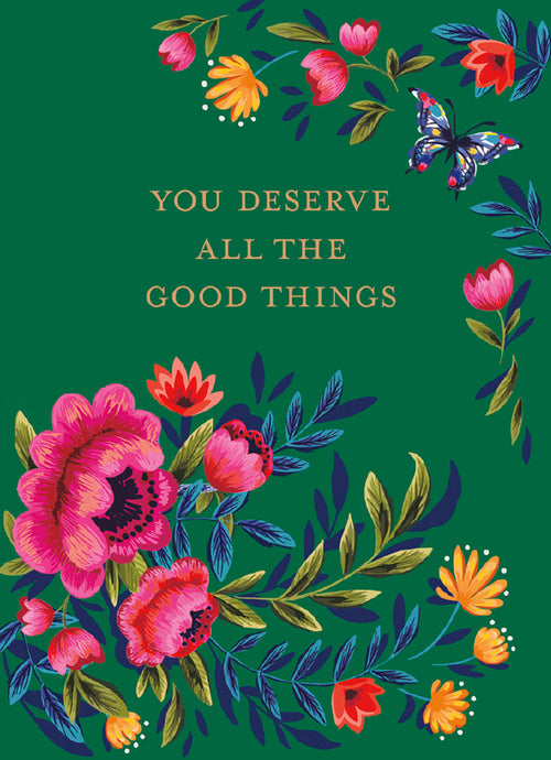 Dark green magnet with gold text "YOU DESERVE ALL THE GOOD THINGS", surrounded by vibrant folk-art style pink, red, and orange flowers, green and blue leaves, and a colorful butterfly in the top right corner. Inspirational fridge magnet with floral design.