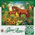 300-piece MasterPieces Green Acres EZ-Grip jigsaw puzzle depicting a brown mare and her foal in a vibrant summer pasture surrounded by sunflowers, butterflies, fruit trees, and wildflowers under a bright blue sky, with MasterPieces logo visible.