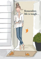Encouraging greeting card featuring a serene woman with a bun, wearing a white shirt and jeans, holding a coffee cup, standing by an open door. Text reads 'Remember, life is tough...'. The setting includes a doormat with autumn leaves and a green potted plant, suggesting a moment of reflection.