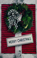 Front of a vibrant festive greeting card featuring a lush green wreath adorned with pinecones and a stylish black and white buffalo check bow, set against a rich red background with a 'MERRY CHRISTMAS' sign.