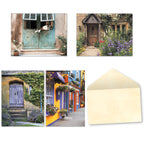 Assortment of four unique blank greeting cards featuring picturesque scenes: a cute dog peeking from an open shuttered window, a charming wooden doorway surrounded by purple flowers, a rustic stone cottage with a blue door and ivy, and a vibrant street scene with colorful buildings.
