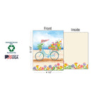Detailed view of a greeting card with a blue bicycle and flowers, showing its 4 1/2 x 5 1/2 inch dimensions, the blank inside, and logos for Sustainably-Sourced Paper, Soy-Based Inks, and Made in USA.