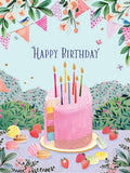 Front of a vibrant, whimsical greeting card featuring a multi-layered pink birthday cake with colorful candles, surrounded by strawberries, macarons, and decorative bunting. Small birds and butterflies flutter around, all against a pastel blue sky with green floral ground. The text 'Happy Birthday' is prominently displayed above the cake.
