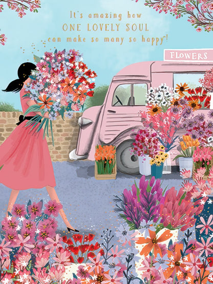 Woman with large floral bouquet walks past a pink flower truck filled with vibrant blossoms and gold flecks. Front of a birthday card.