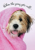 Adorable shaggy brown and white puppy dog wrapped snugly in a soft pink towel, with its tongue slightly out, against a light pink background. Text reads 'When the going gets ruff...'. Perfect for a sympathy or support card.