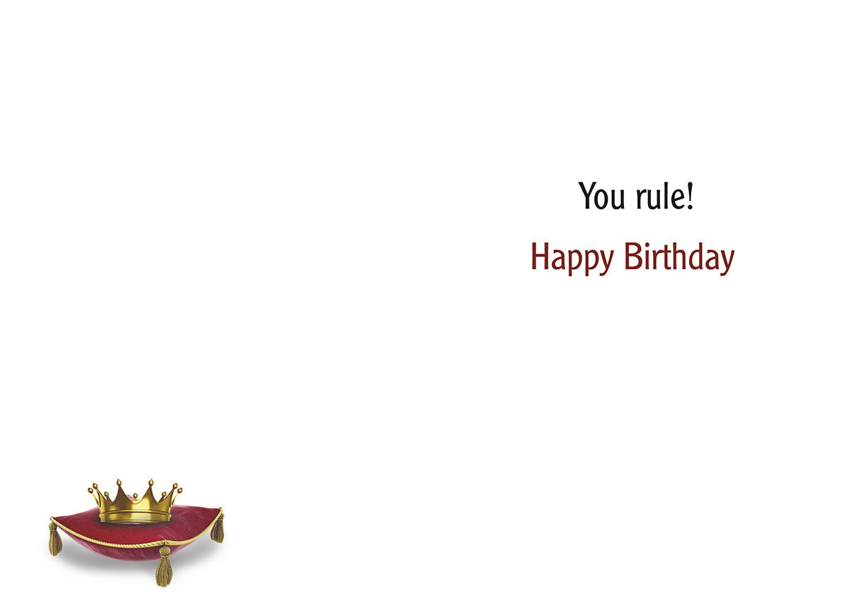 Inside of a humorous birthday greeting card with white background, text 'You rule! Happy Birthday', and a small gold crown on a red velvet cushion.