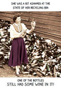 Funny greeting card front featuring a retro woman in a purple skirt and striped shirt, holding a wine bottle amidst a large pile of empty bottles. Text reads: 'SHE WAS A BIT ASHAMED AT THE STATE OF HER RECYCLING BIN ONE OF THE BOTTLES STILL HAD SOME WINE IN IT!'. Perfect humor for a woman's special day.