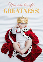 Adorable baby boy wearing a golden crown and red royal cape, lying on a white satin sheet, with elegant text 'You were born for GREATNESS!' Perfect encouraging card for a child's special day.