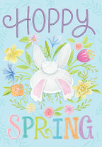 Cute Easter card front featuring a fluffy white bunny tail and pink feet emerging from vibrant spring flowers like daffodils, tulips, and cornflowers, with 'HOPPY SPRING' text on a light blue background.