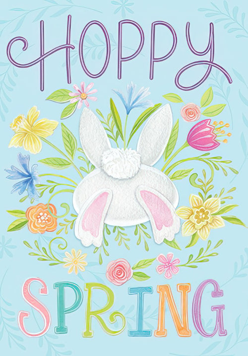 Cute Easter card front featuring a fluffy white bunny tail and pink feet emerging from vibrant spring flowers like daffodils, tulips, and cornflowers, with 'HOPPY SPRING' text on a light blue background.