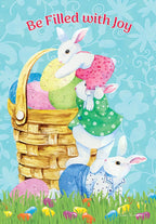 Front of a vibrant Easter greeting card featuring three cute white bunnies, a golden basket overflowing with pastel colored eggs, and the joyful text 'Be Filled with Joy' on a light blue background with a green grassy foreground adorned with small colorful eggs.