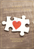 Romantic Valentine's Day greeting card featuring two interlocking puzzle pieces forming a vibrant red heart, with the message 'We'll always be a perfect fit' and 'Happy Valentine's Day' text against a rustic wooden background with a gold border. Perfect for a spouse or partner.
