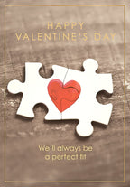 Romantic Valentine's Day greeting card featuring two interlocking puzzle pieces forming a vibrant red heart, with the message 'We'll always be a perfect fit' and 'Happy Valentine's Day' text against a rustic wooden background with a gold border. Perfect for a spouse or partner.