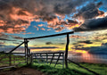 Scenic landscape greeting card featuring a rustic wooden gate and fence at sunset, vibrant orange and blue clouds, and a calm ocean vista, perfect for thoughtful messages.
