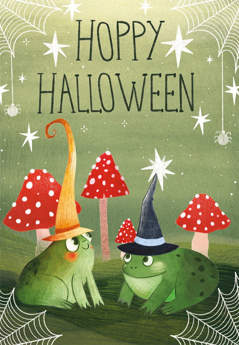 Front of a cute spooky season greeting card featuring two cartoon frogs wearing pointy wizard hats, surrounded by red spotted mushrooms and delicate spiderwebs on a green background. Text reads 'HOPPY HALLOWEEN'.