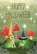 Front of a cute spooky season greeting card featuring two cartoon frogs wearing pointy wizard hats, surrounded by red spotted mushrooms and delicate spiderwebs on a green background. Text reads 'HOPPY HALLOWEEN'.