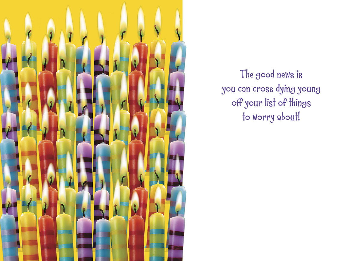 Inside of a humorous birthday card showing a dense arrangement of lit colorful striped candles on the left side, with a witty message on the right: 'The good news is you can cross dying young off your list of things to worry about!'