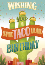 Front of a funny greeting card featuring a large green cactus with three birthday tacos topped with candles and confetti. Text reads 'Wishing you a Spec-TACO-ular Birthday' with wrapped gifts at the base in a desert scene.