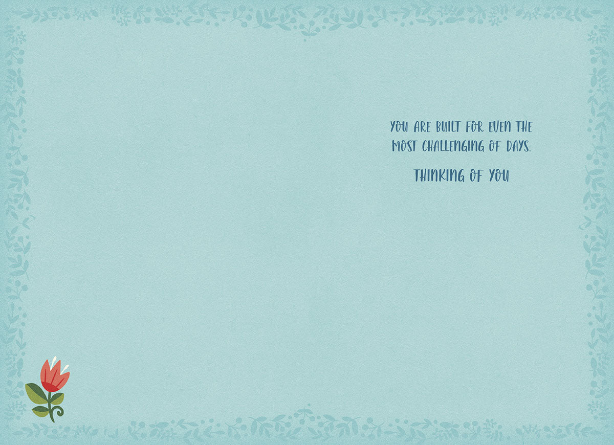 Inside of inspiring greeting card with light blue background and message 'YOU ARE BUILT FOR EVEN THE MOST CHALLENGING OF DAYS. THINKING OF YOU.' with a small red folk art flower in the corner.