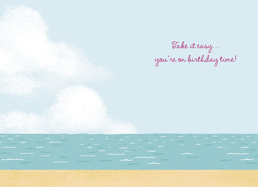 Inside of a tropical birthday card showing a serene ocean and beach scene with white clouds and sandy beach with text 'Take it easy... you're on birthday time!'
