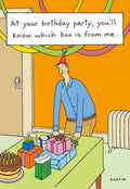 Funny adult birthday card front featuring a man in a party hat, standing next to a table laden with a chocolate cake, various wrapped gifts, and a green gift bag. The humorous text reads: 'At your birthday party, you'll know which box is from me.'