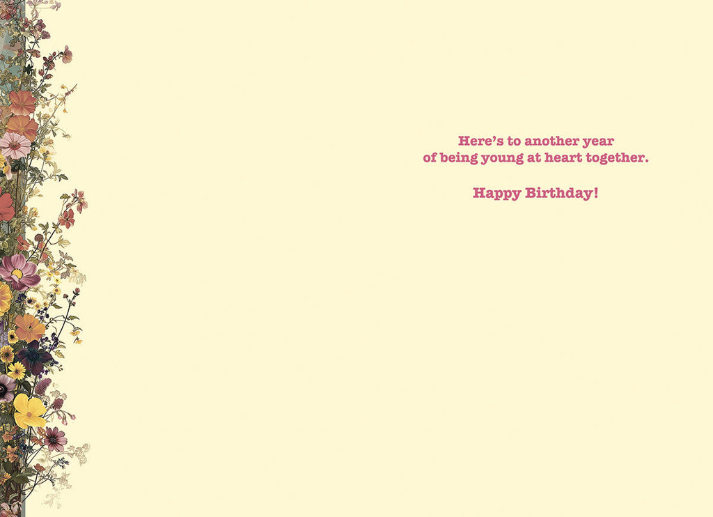 Inside of a lighthearted birthday card for a sister, showing a cream background with a decorative floral border on the left, and the message 'Here's to another year of being young at heart together. Happy Birthday!'