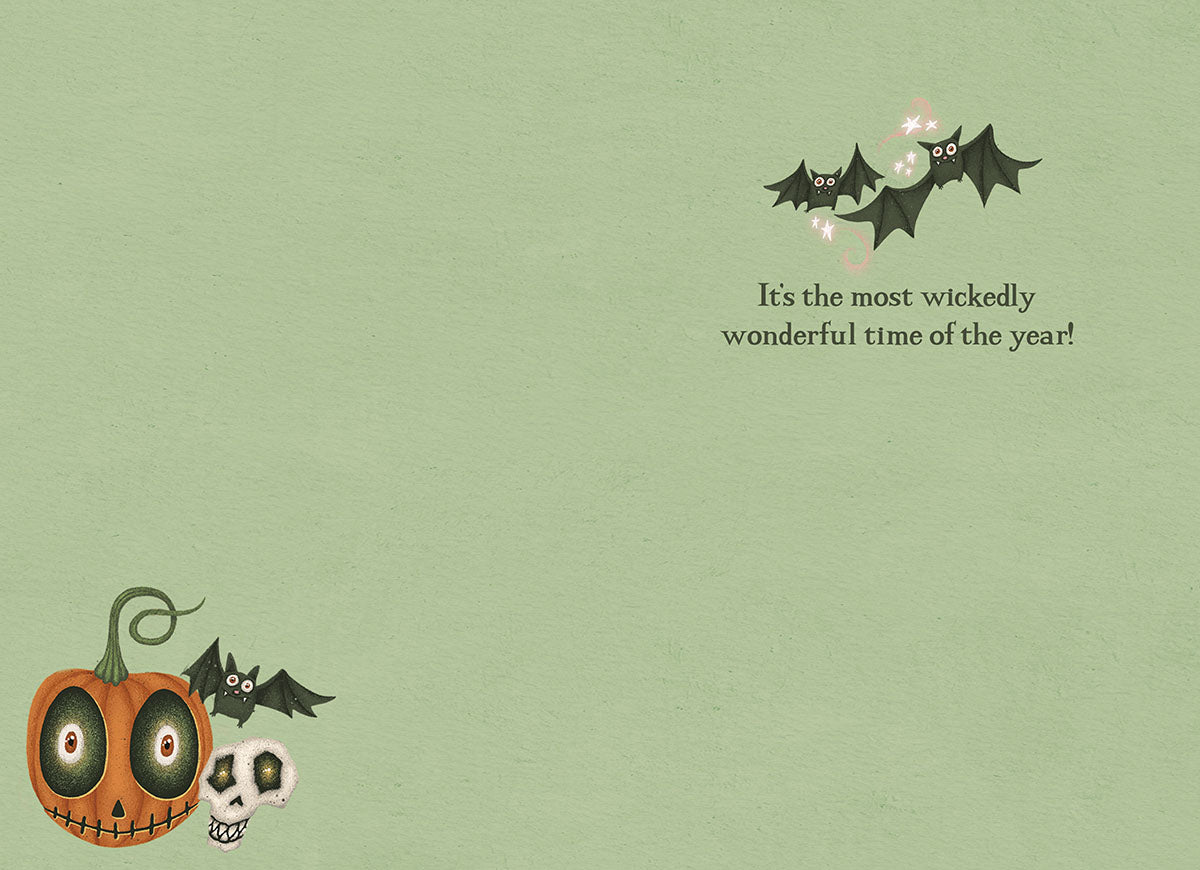 Inside of a cute Halloween greeting card, showing flying bats, a small pumpkin and skull illustration, with the message 'It's the most wickedly wonderful time of the year!' on a pale green background.