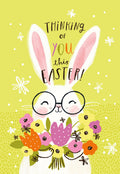 Cute white bunny wearing round glasses, holding a vibrant spring flower bouquet on a yellow background, with 'Thinking of you this Easter!' text. Ideal Easter greeting card for kids and family.