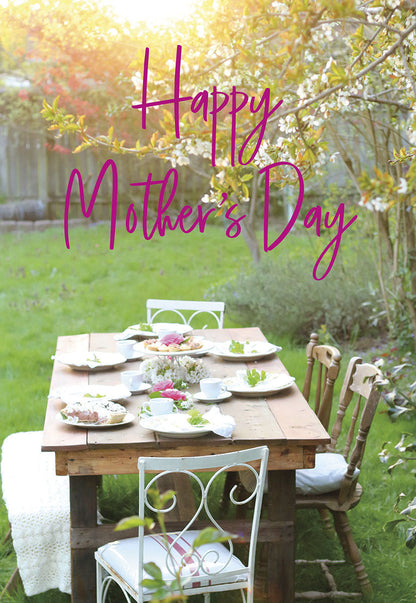 Happy Mother's Day card with an outdoor table set with plates of pie and blooming flowers in golden sunlight.