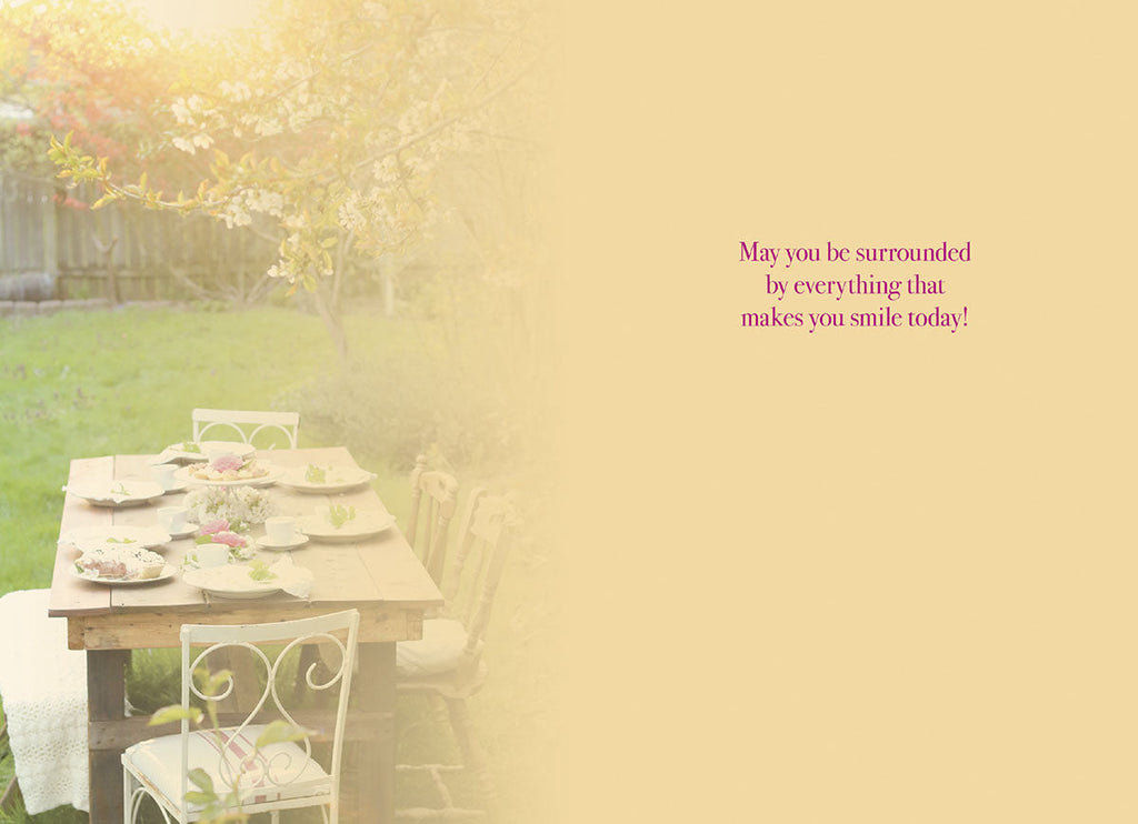 Inside of a greeting card with a heartfelt message, 'May you be surrounded by everything that makes you smile today!', against a soft outdoor garden setting.