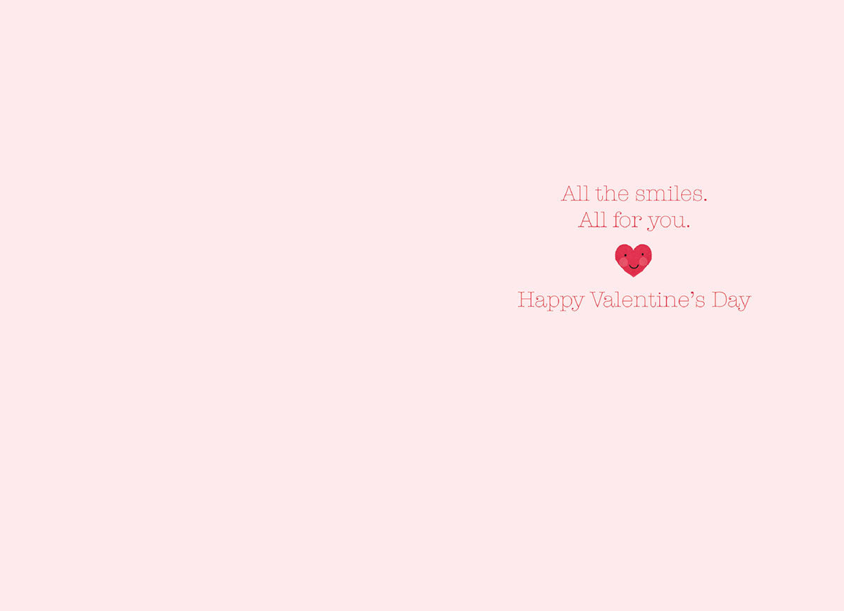 Inside of a light pink greeting card with text 'All the smiles. All for you.' and 'Happy Valentine's Day' accompanied by a small smiling red heart illustration.