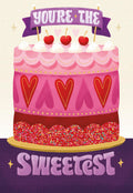 Front of a romantic Valentine's Day greeting card featuring a multi-tiered pink and red cake illustration with heart decorations, colorful sprinkles, and three red cherries on top, with a banner reading 'You're the Sweetest'.