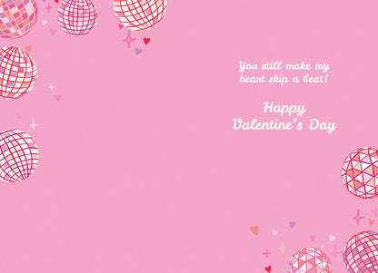 Inside of a pink greeting card with disco balls, hearts, and text 'You still make my heart skip a beat! Happy Valentine's Day'.
