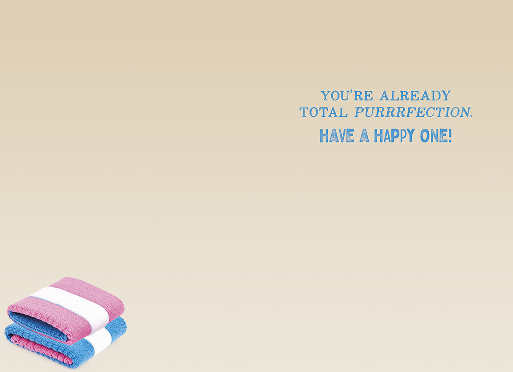 Inside of a light beige greeting card featuring the blue text 'YOU'RE ALREADY TOTAL PURRRFECTION. HAVE A HAPPY ONE!' with two small folded pink and blue towels in the corner, conveying a cute and complimentary birthday wish.