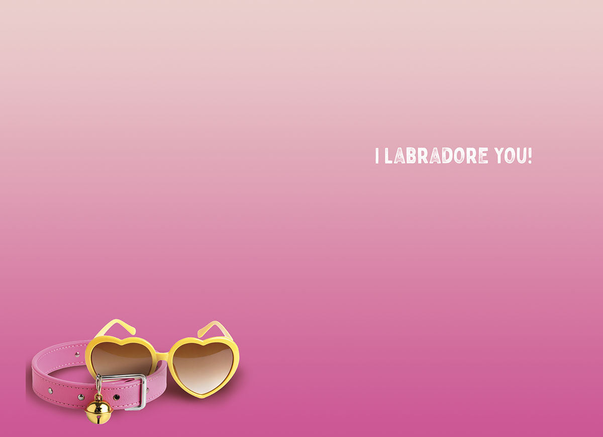 A pink dog collar with a gold bell and matching yellow heart-shaped sunglasses resting on a pink gradient background. The card's inside message "I LABRADORE YOU!" is visible.