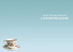Inside of a light blue greeting card showing a small floral teacup and saucer in the bottom left. The message 'HOPE YOU'RE FEELING A LITTLE BETTER EACH DAY.' is centered on the right side.