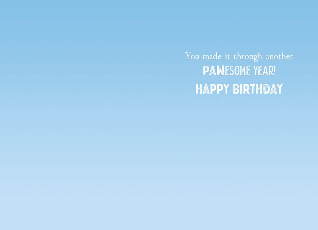 Inside of a humorous greeting card with a light blue sky background, displaying the message 'You made it through another PAWESOME YEAR! HAPPY BIRTHDAY' in playful white font.