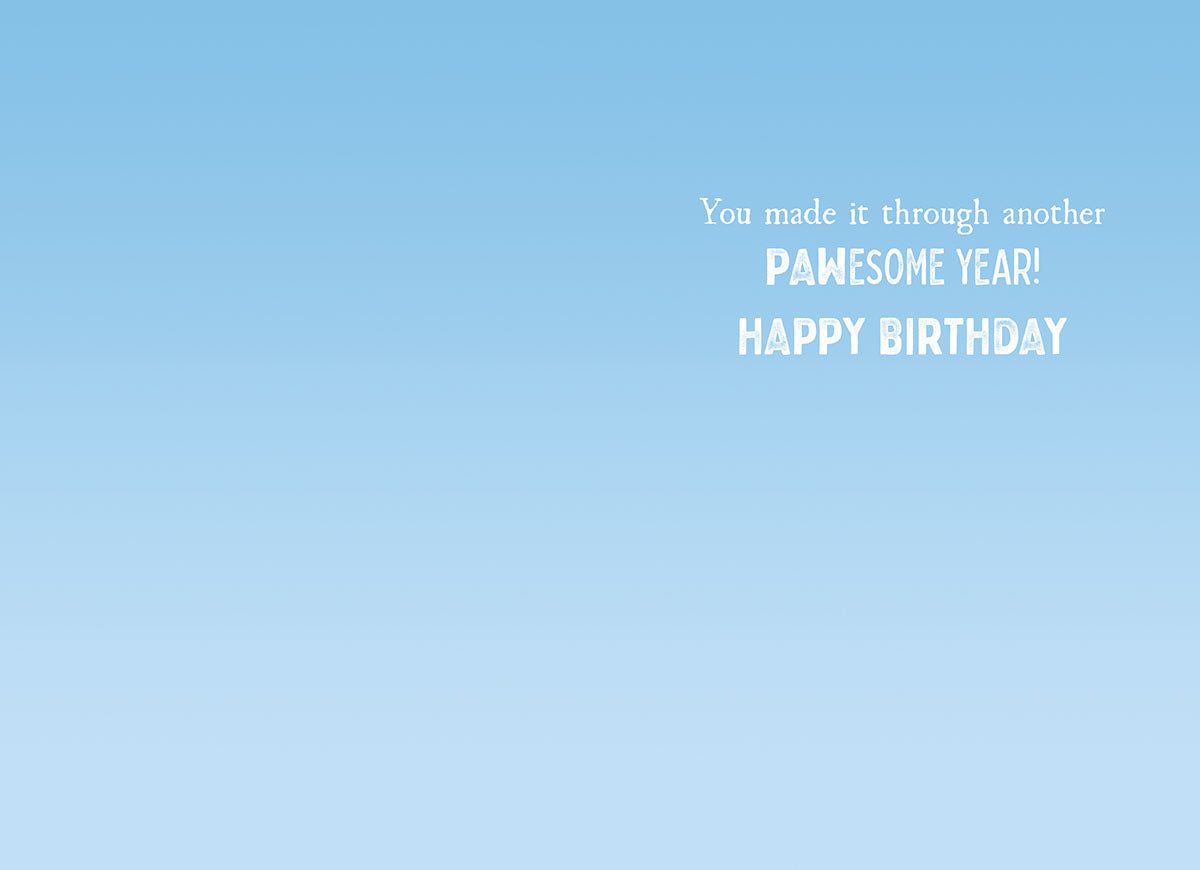 Inside of a humorous greeting card with a light blue sky background, displaying the message 'You made it through another PAWESOME YEAR! HAPPY BIRTHDAY' in playful white font.