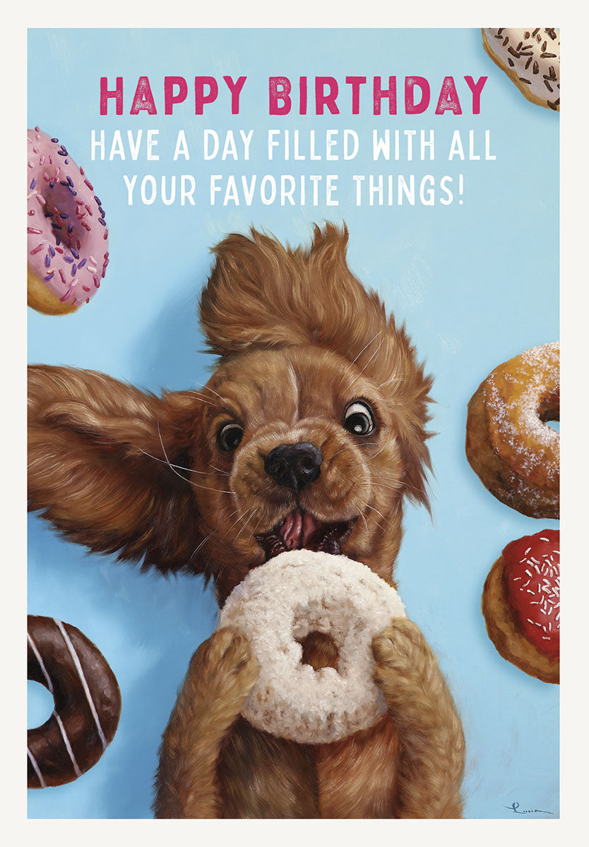 Front of a vibrant blue greeting card featuring an excited brown cocker spaniel puppy with floppy ears, gleefully holding a white frosted donut. Various colorful donuts with sprinkles are scattered around the playful dog. Bold pink text reads "HAPPY BIRTHDAY HAVE A DAY FILLED WITH ALL YOUR FAVORITE THINGS!".