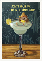 Funny lighthearted greeting card featuring a whimsical illustration of a cute hedgehog wearing a straw sombrero, relaxing in a green margarita glass with a lime slice, set against a dark teal background with white cactus patterns. The card's front reads: 'TODAY'S YOUR DAY TO BE IN THE LIMELIGHT!'. Ideal for celebrating a friend's special day.