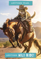 Front of a funny greeting card featuring a tabby cat in a cowboy hat riding a bucking horse in a desert landscape. Text reads 'ANOTHER YEAR... ANOTHER WILD RIDE!'