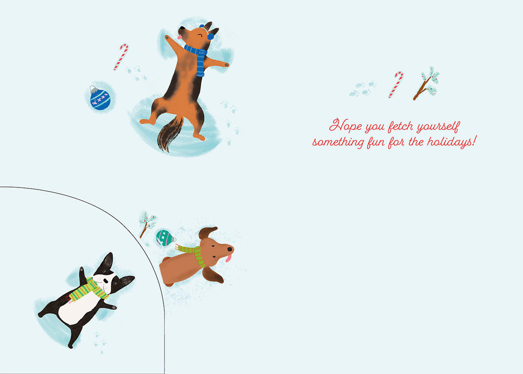 Inside of a light blue greeting card, featuring two playful cartoon dogs making snow angels, a candy cane, and a small blue ornament. The text "Hope you fetch yourself something fun for the holidays!" is written in red script on the right side. A partial view of a third dog is visible in the bottom left corner.