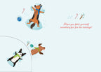 Inside of a light blue greeting card, featuring two playful cartoon dogs making snow angels, a candy cane, and a small blue ornament. The text "Hope you fetch yourself something fun for the holidays!" is written in red script on the right side. A partial view of a third dog is visible in the bottom left corner.