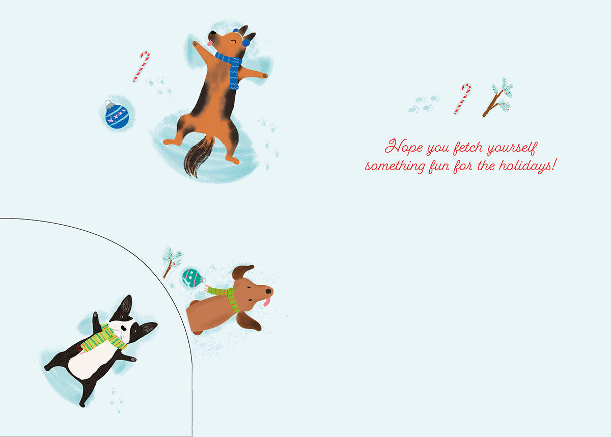 Inside of a light blue greeting card, featuring two playful cartoon dogs making snow angels, a candy cane, and a small blue ornament. The text "Hope you fetch yourself something fun for the holidays!" is written in red script on the right side. A partial view of a third dog is visible in the bottom left corner.