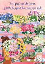 Greeting card cover featuring an illustrated woman holding a bouquet at a vibrant flower market, surrounded by colorful blooms. Text reads: 'Some people are like flowers... just the thought of them makes you smile.'