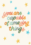 Front of an inspiring graduation greeting card featuring colorful text 'You are capable of amazing things' surrounded by gold and blue stars on a light cream background, perfect for celebrating success.