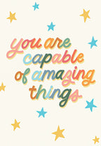 Front of an inspiring graduation greeting card featuring colorful text 'You are capable of amazing things' surrounded by gold and blue stars on a light cream background, perfect for celebrating success.