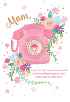 Front of a Mother's Day greeting card featuring a pink vintage rotary telephone, surrounded by colorful watercolor flowers in pink, blue, purple, and yellow. The text "Mom," is written above the phone, and below it reads: "You're the first person I want to tell when something happens that's really great or really hard."