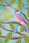 Cute Mother's Day greeting card featuring a whimsical colorful bird wearing a golden crown, perched on a tree branch with green leaves and pink and blue flowers, with the text 'You Rule!' in sparkling yellow font on a light blue background. Perfect for a queen mom.